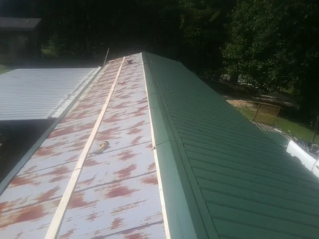 Old rusted panels beside newly installed green metal roofing — Wind Damage Roof Repair by Roofing Brothers in Gansevoort