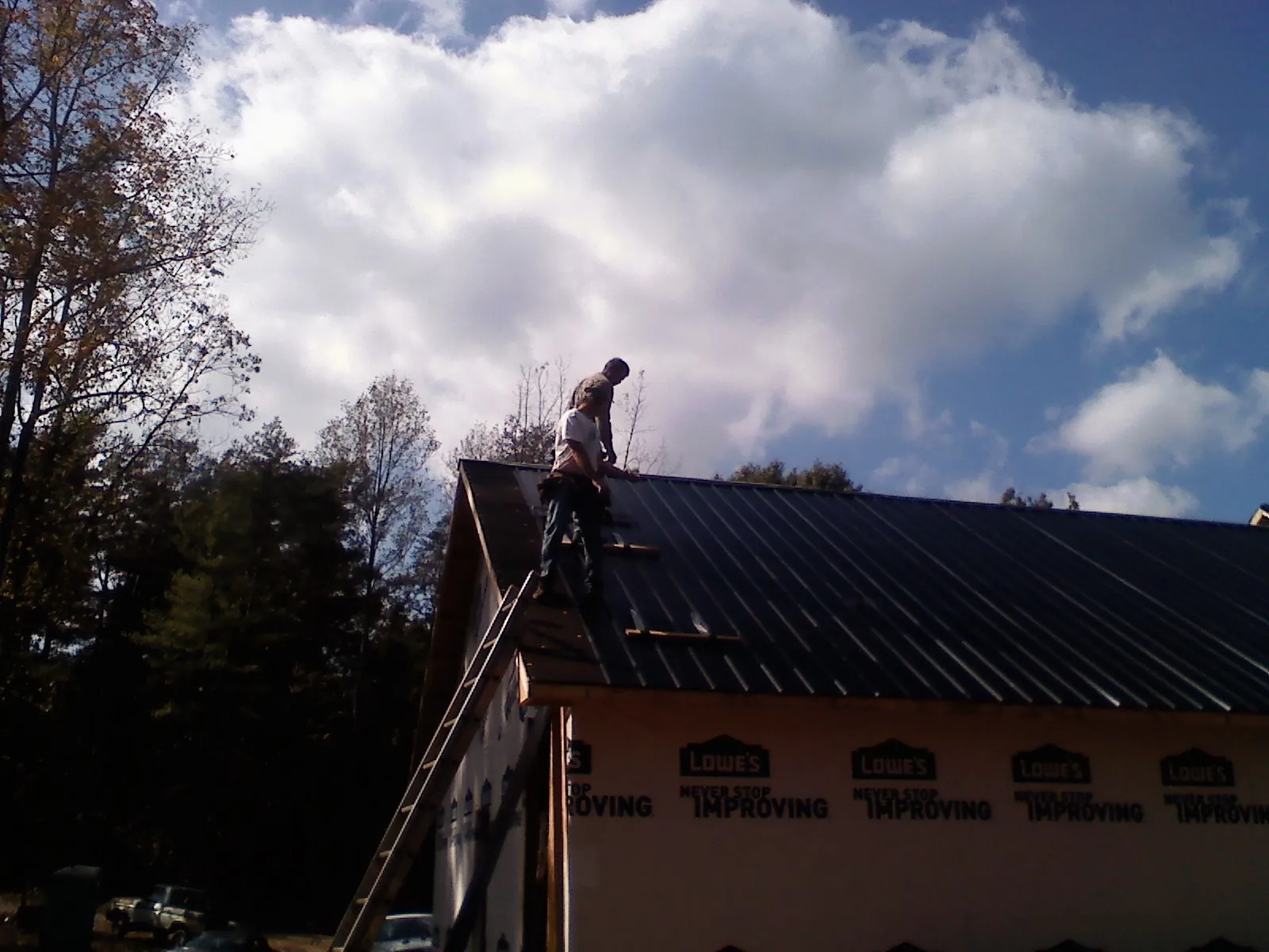 Roofer fastening dark metal panels high against a cloudy sky, from a Roof Inspection job in Gansevoort