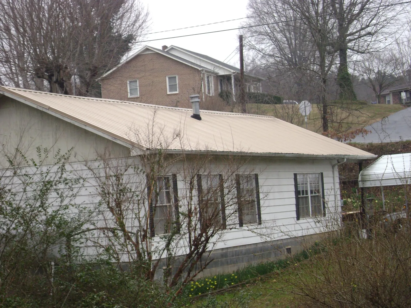 Tan metal roof on a white sided house set into a hillside — Commercial Roofing by Roofing Brothers in Gansevoort